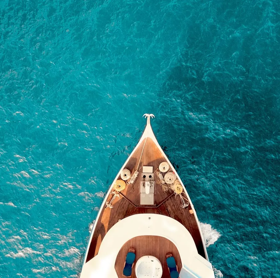 A yacht cutting through turquoise water, seen from above.